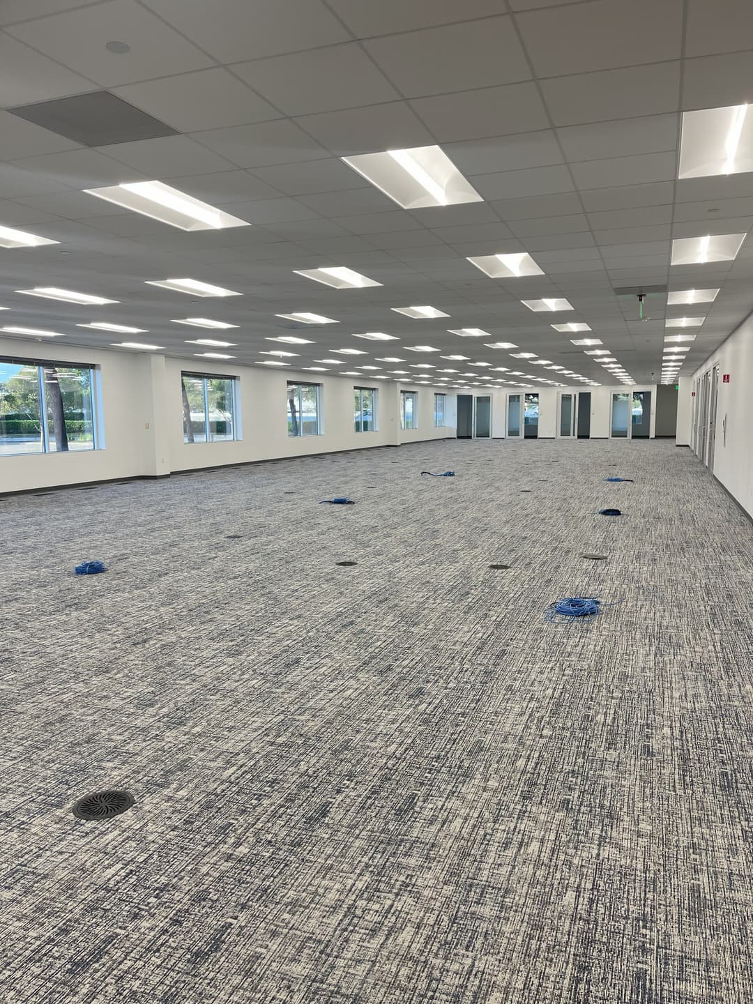 Empty office space with blue floor plugs and large windows, featuring modern carpet and ceiling lights.